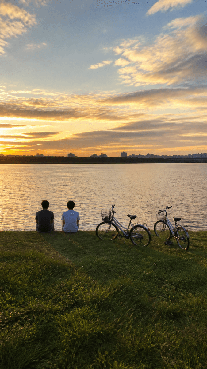 Two people sitting by a river at sunset with their bicycles — natural capture